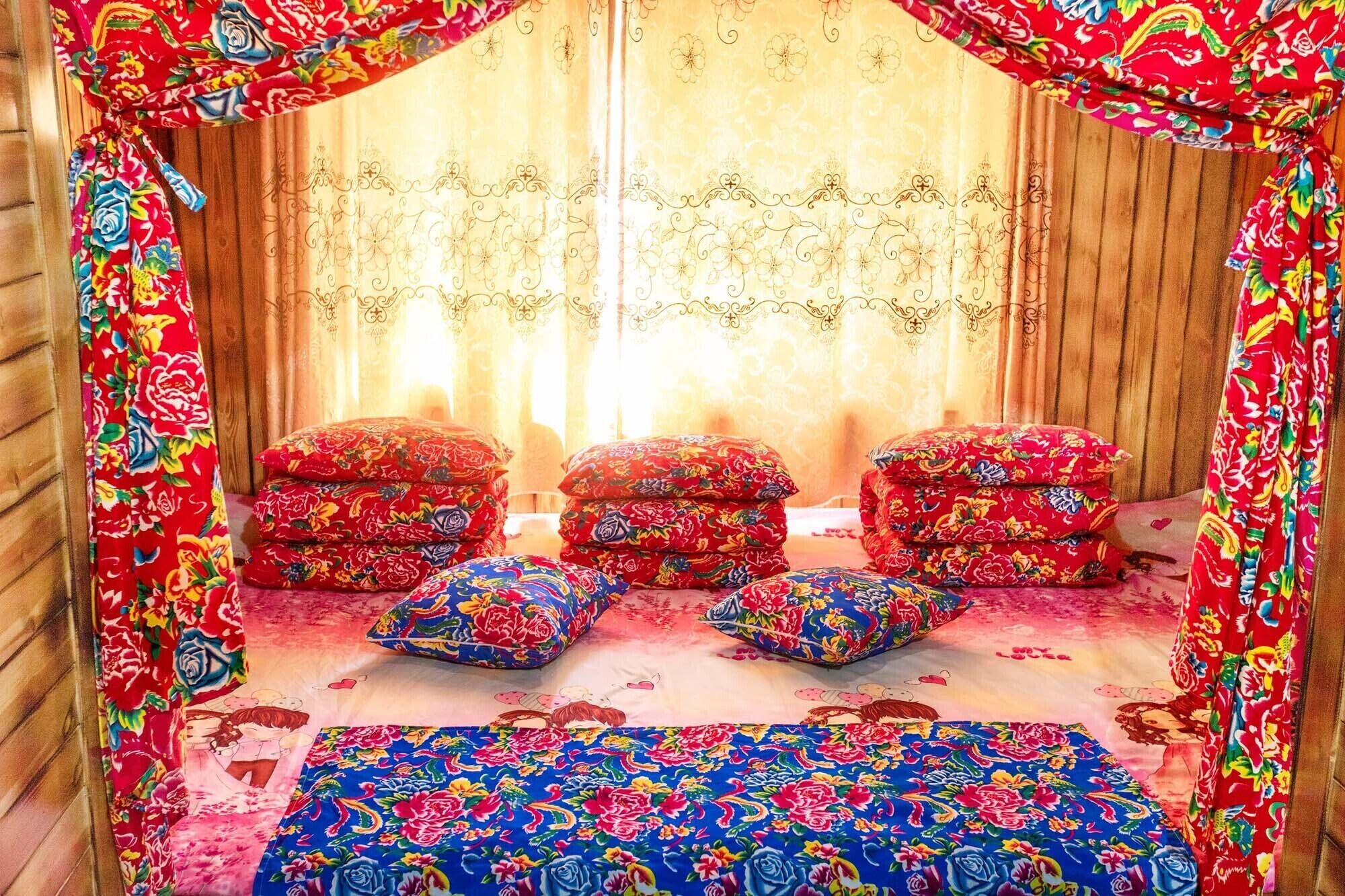 A cozy room with a wooden floor, floral-patterned curtains, and a bed with matching pillows and a blue bedspread.
