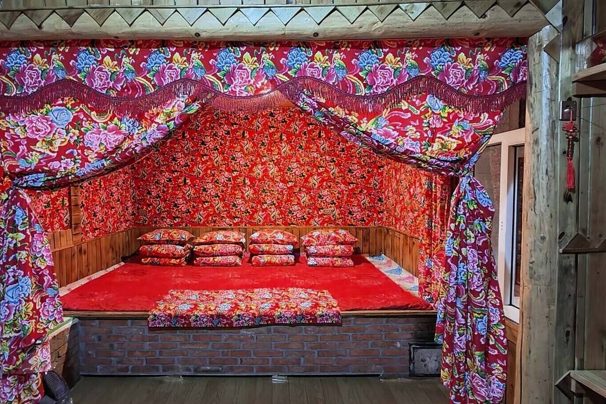 Una habitación rústica y acogedora de madera con piso de ladrillo, una cama de madera con ropa de cama roja y cortinas florales.