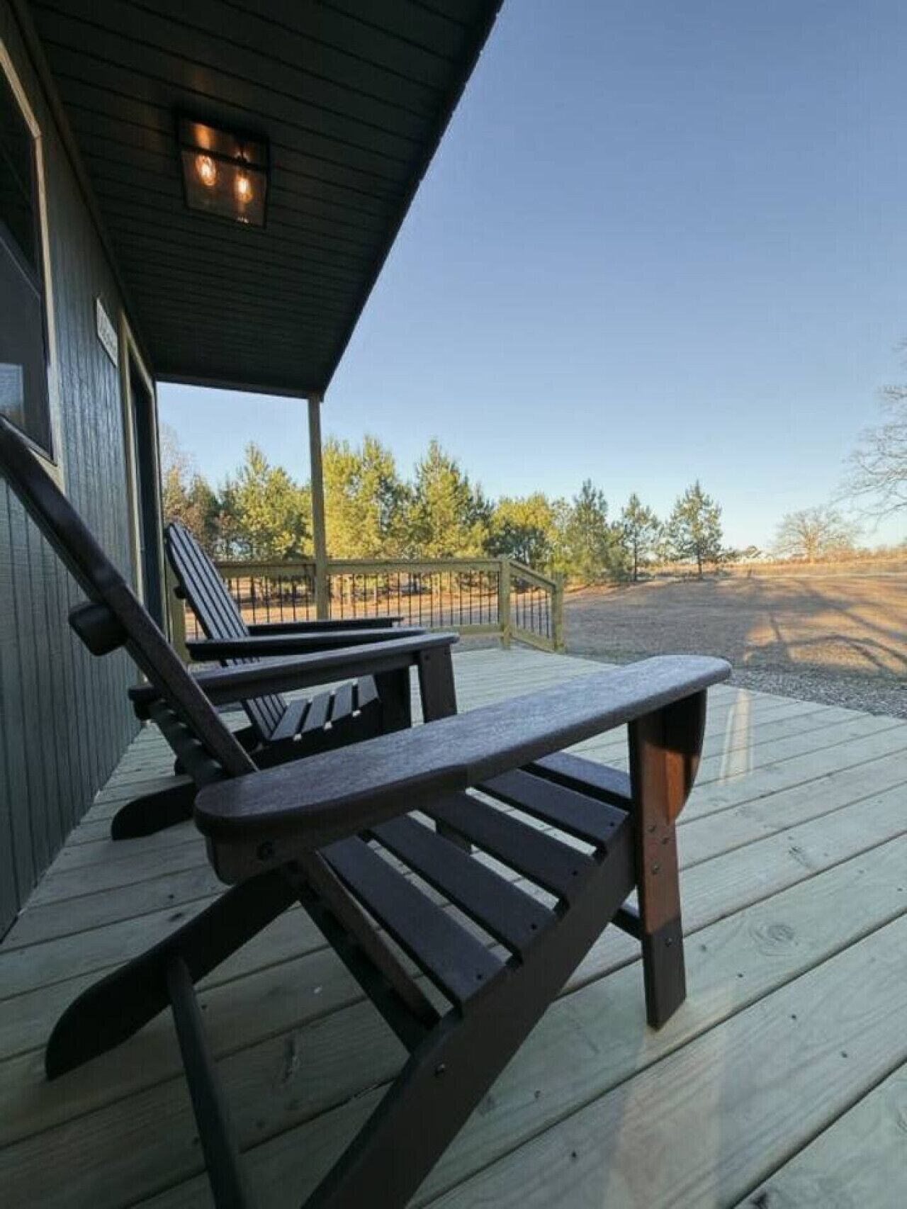 A wooden deck with two lounge chairs and a small table, overlooking a natural landscape with trees and a clear sky.