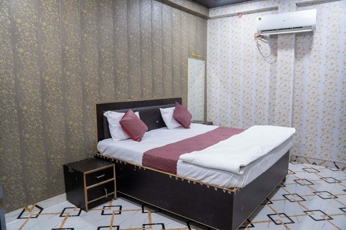 A neatly made bed with a headboard, a bedside table with drawers, and an air conditioning unit mounted on the wall.
