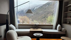 A cozy room with a large window offering a mountain view, a comfortable seating area, and a small table with a lamp.