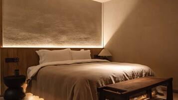 A modern bedroom with a large bed, bedside table, and a round table with a teapot.