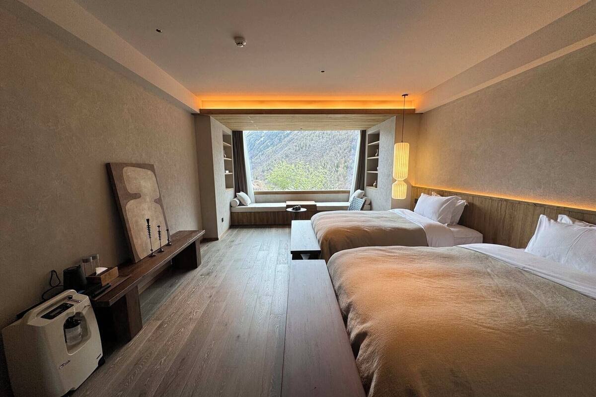 Una habitación de hotel moderna con una cama grande, un banco, una mesita y vistas al exterior.