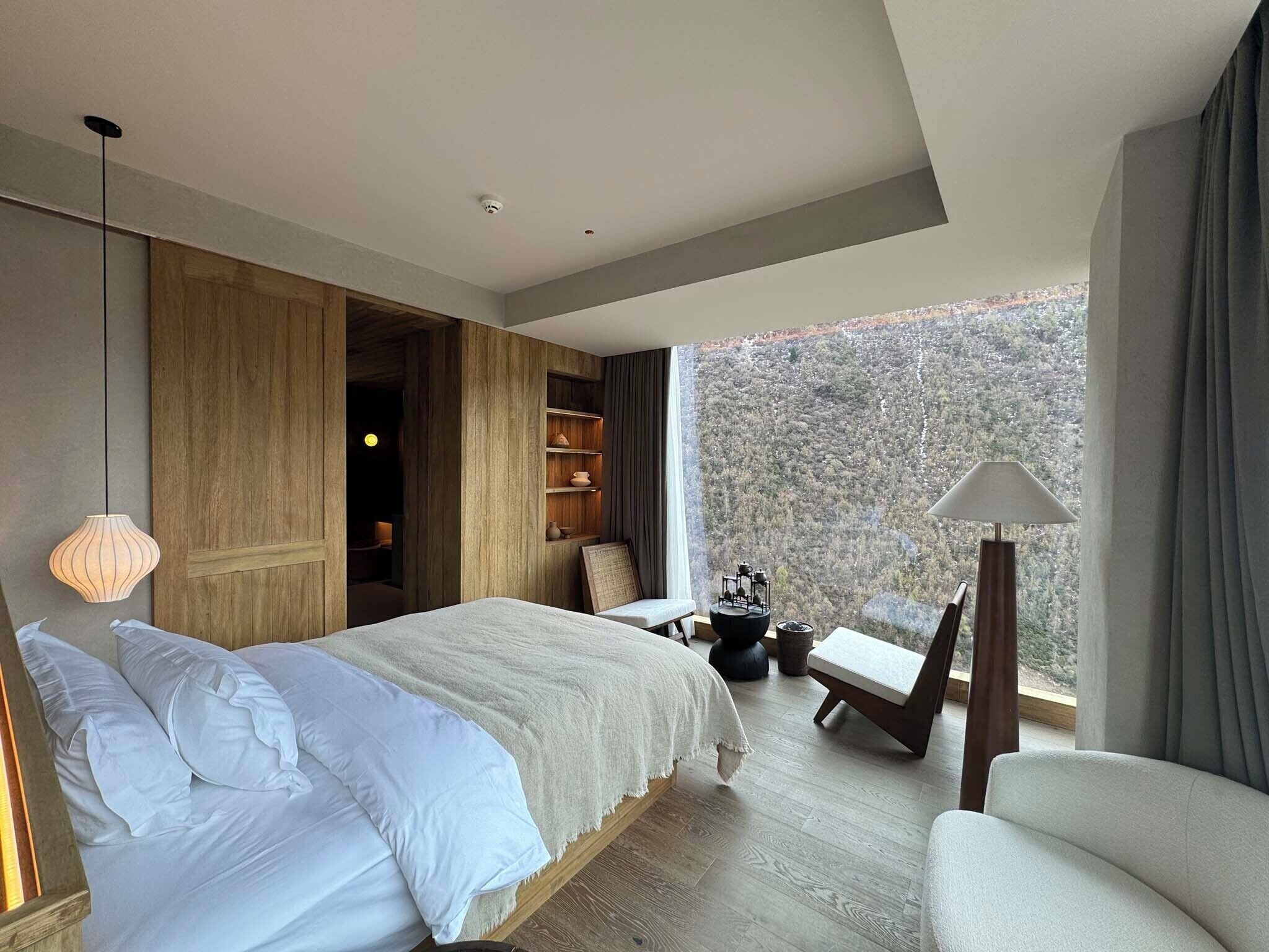 Une chambre moderne dotée d’un grand lit, d’un coin salon et offrant une vue sur un paysage boisé.