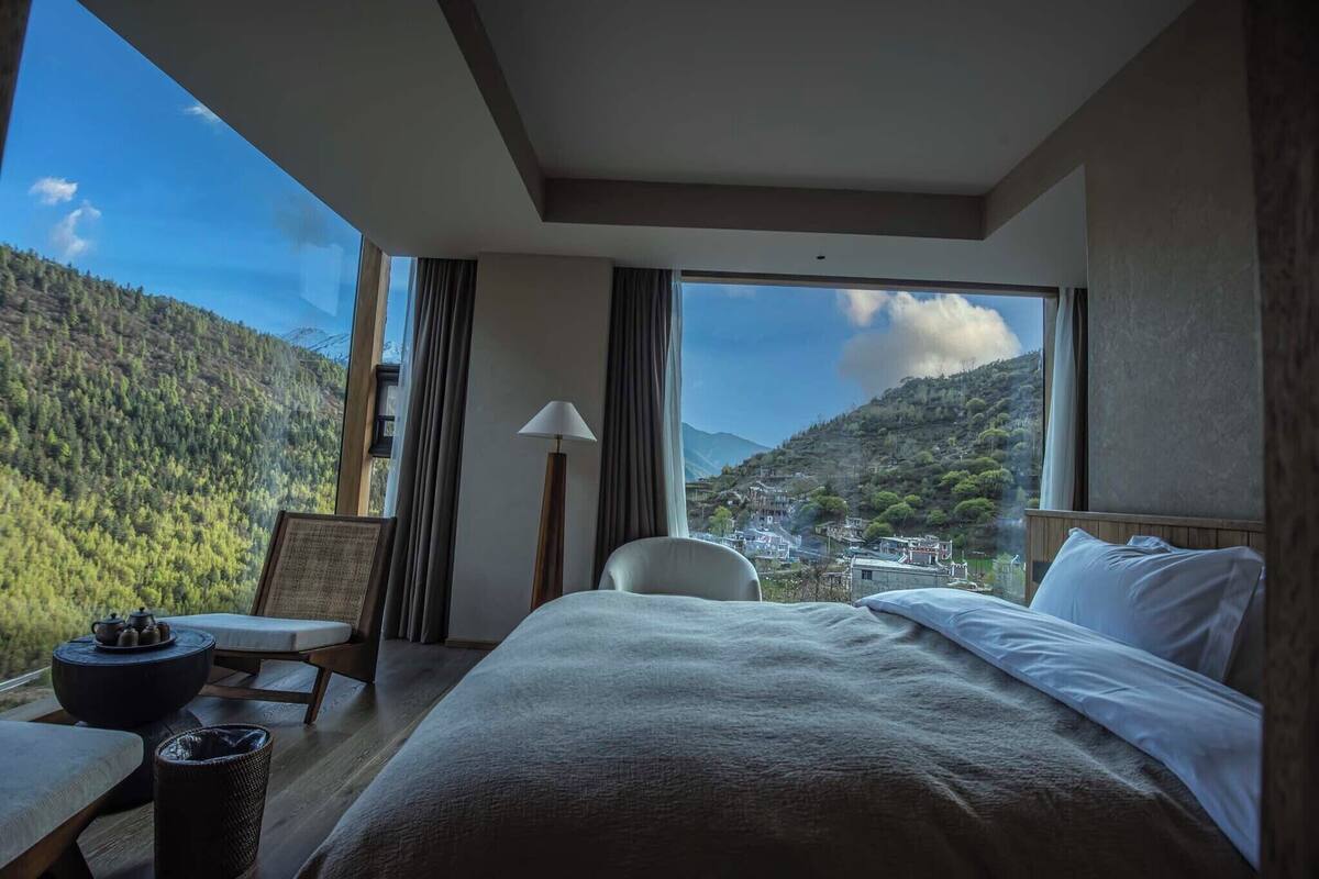 Habitación de hotel con una cama grande, una silla, una mesa y vistas a un paisaje montañoso.