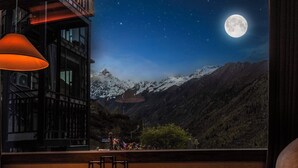 A room with a large window overlooking a mountainous landscape at night, featuring a prominent full moon.