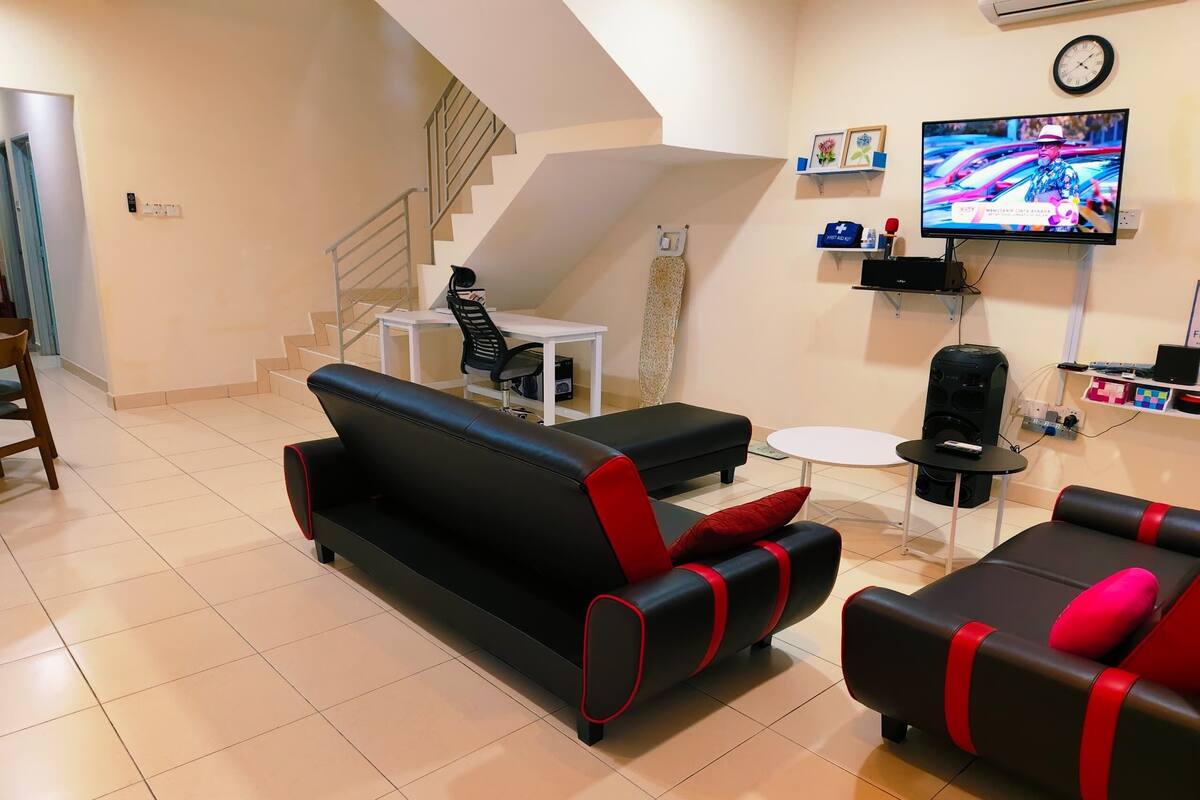 A modern living room with a black sofa, a smaller black sofa with red accents, a white coffee table, and a TV mounted on the wall.