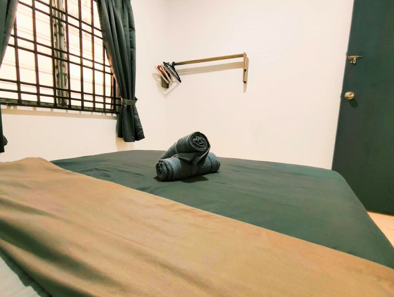 A single bed with a green mattress and a brown blanket, a window with metal bars, and a door with a handle.