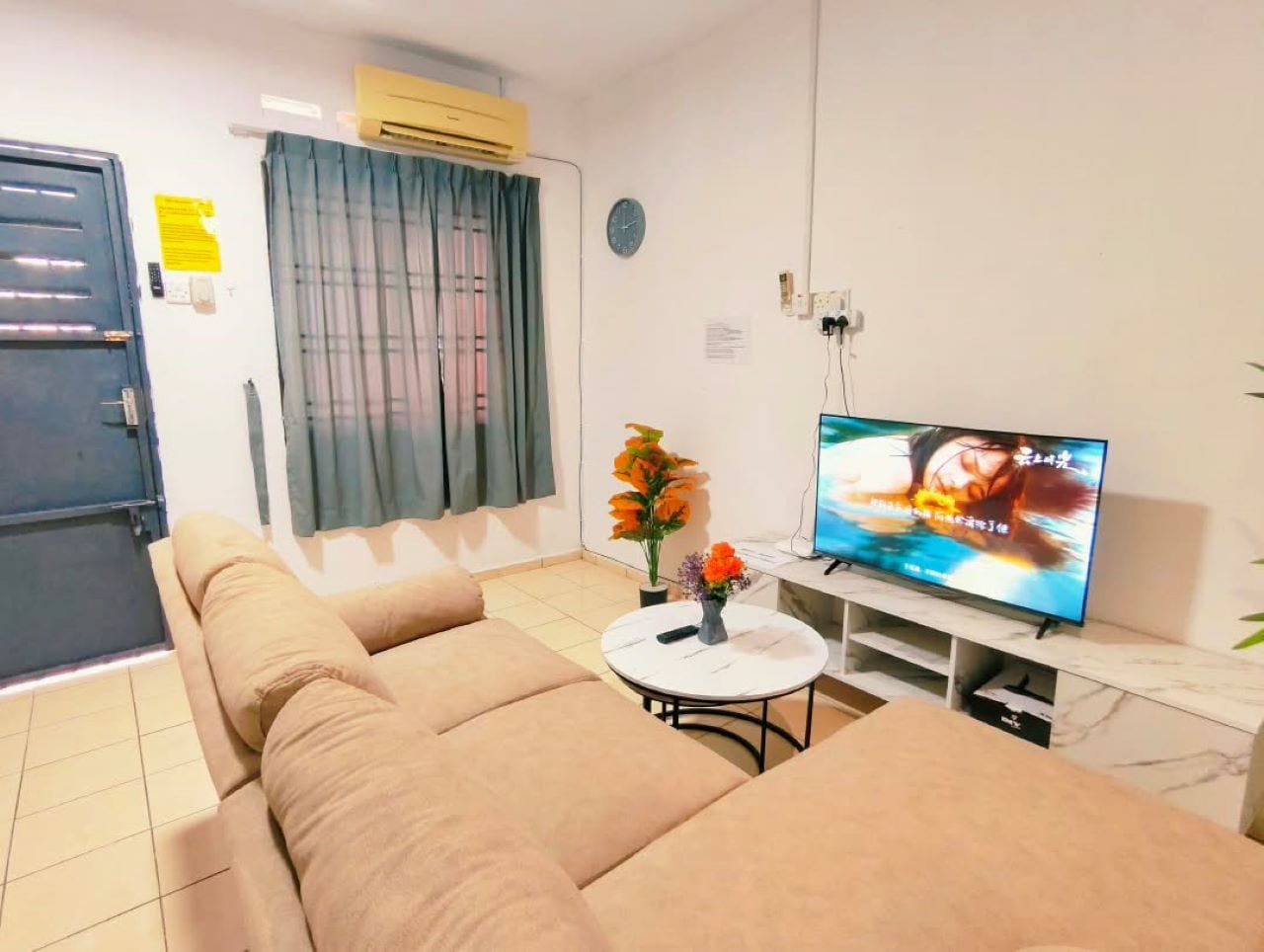 A living room with a sofa, a coffee table with flowers, a TV, and a door.
