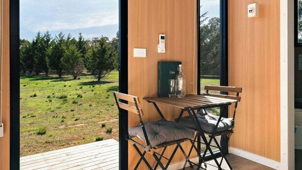 Quarto moderno com mesa e cadeiras de madeira, vista para um campo gramado e uma janela grande.