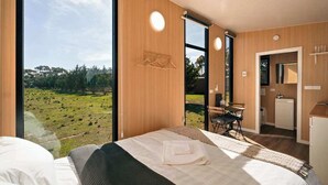 Quarto com uma janela grande, uma cama, uma escrivaninha e uma pequena cozinha.
