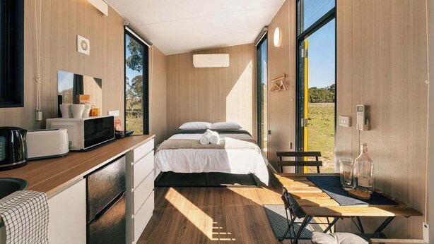 Een moderne, compacte kamer met een bed, kitchenette en grote ramen met uitzicht op de omgeving.