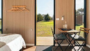 Een slaapkamer met een bed, een tafel met stoelen en uitzicht op een gazon door een groot raam.