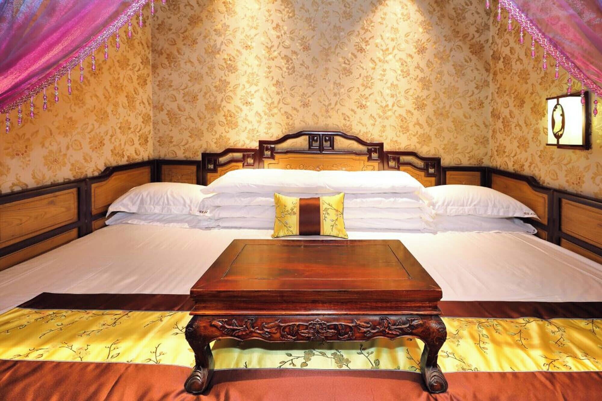 Une chambre à coucher avec un lit en bois, du linge de lit blanc, une table de chevet en bois et un papier peint à motifs floraux.