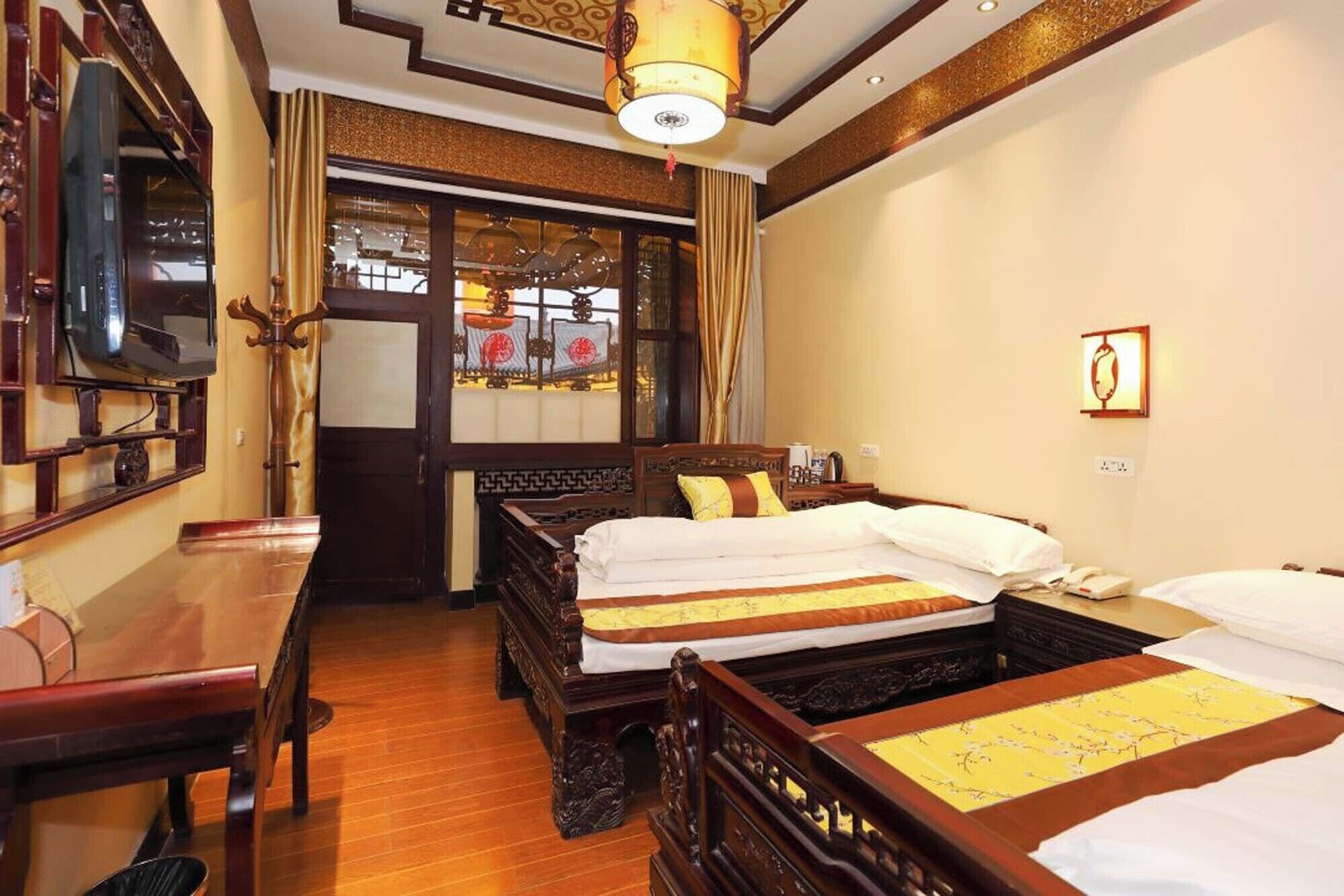 A traditional room with two wooden beds, a desk, and a television.