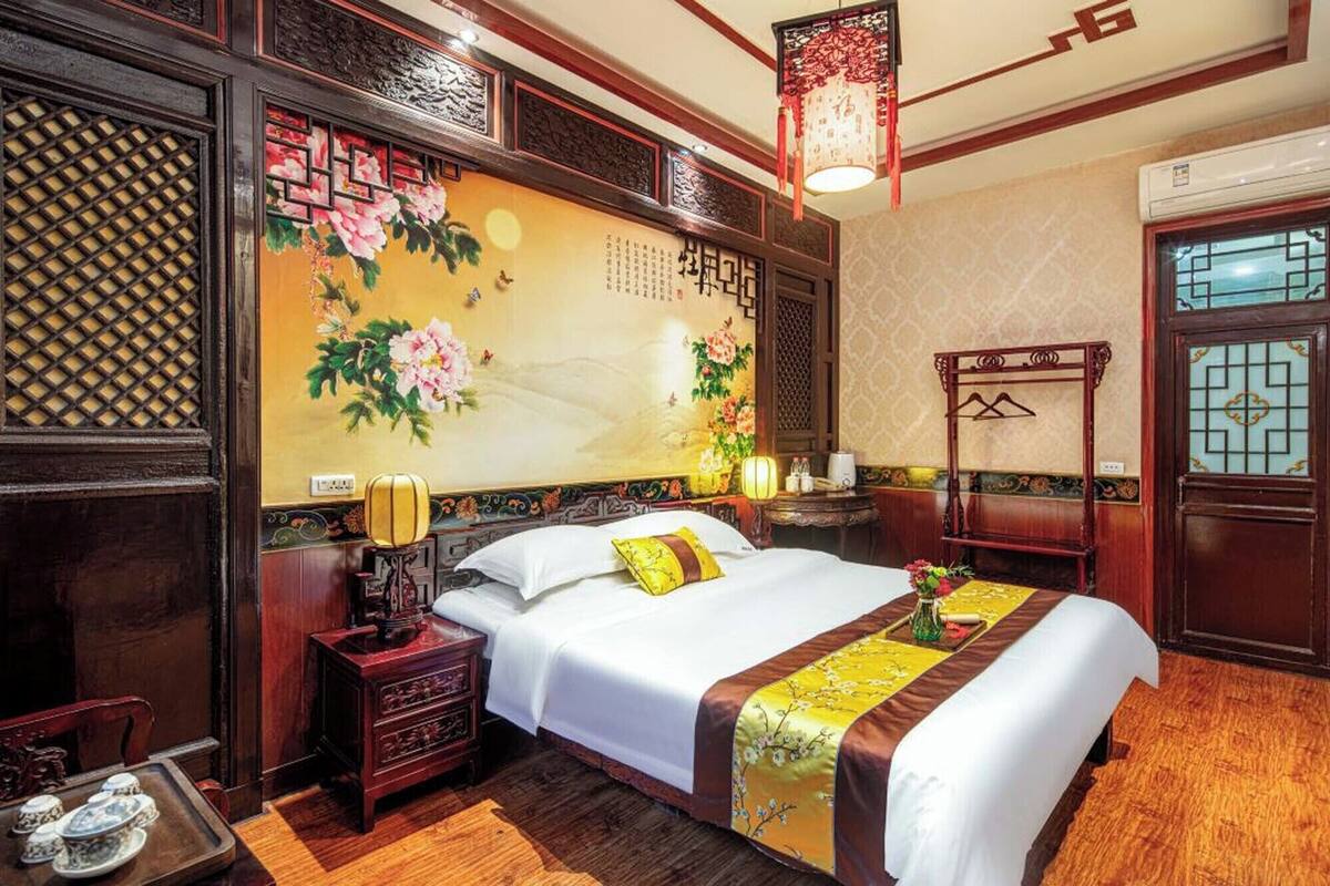 Ein traditionell eingerichtetes Hotelzimmer mit einem großen Bett, Holzmöbeln und einer Wand mit floralen Bildern.