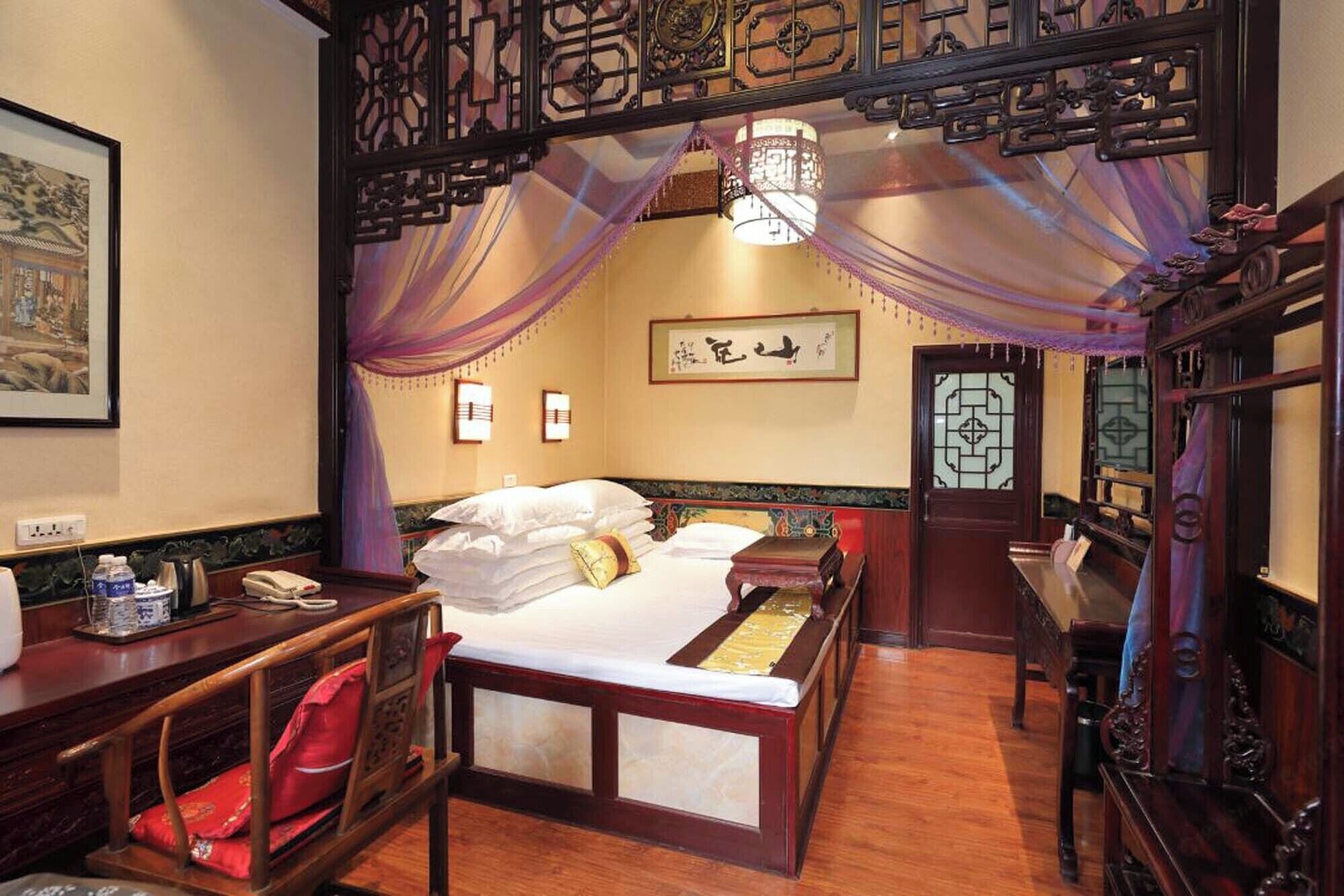 A traditional room with a bed, a desk, and a chair. There is a decorative screen above the bed and a wall-mounted light fixture.
