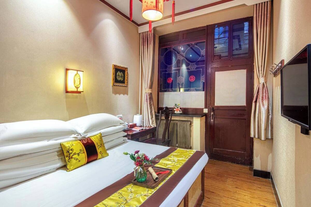 Ein Hotelzimmer mit Bett, Nachttisch, Lampe und Blick ins Freie durch ein Fenster.