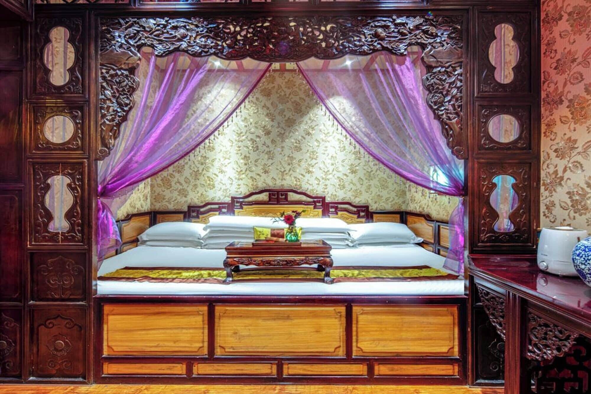 A traditional bed with a canopy, wooden headboard, and a bedside table with a vase.