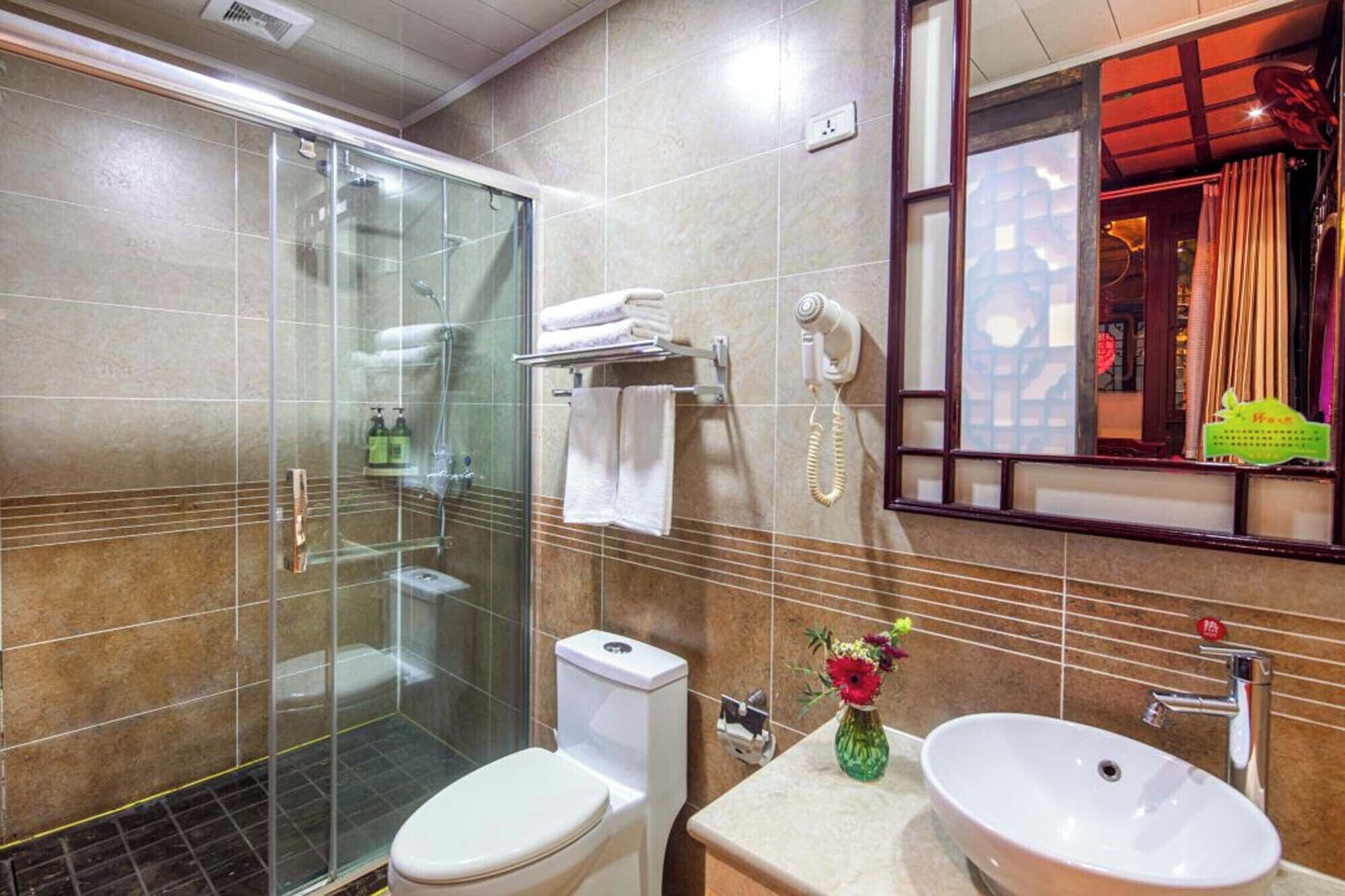 Een moderne badkamer met een douchecabine van glas, een toilet, een wastafel met een bloevas en een telefoon.