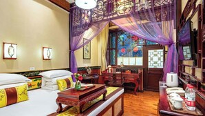 A traditional room with a bed, a wooden table with a tray, and a desk with a telephone and water bottles. - PingYao ChengJia Laoyuan Hotel (Jinzhong)