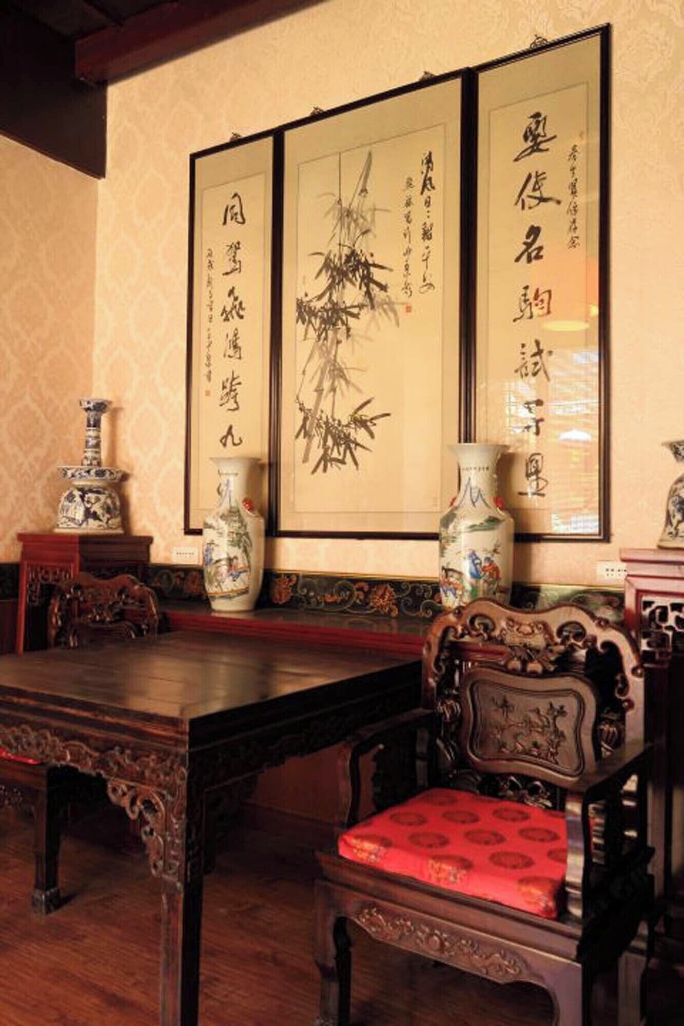 A traditional room with a wooden table and chairs, a vase, and calligraphy on the wall.
