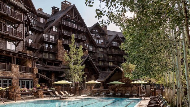 A multi-story wooden building with a swimming pool and lounge chairs.