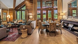 A spacious living room with a fireplace, a dining area with a chandelier, and large windows offering a view of the outdoors.