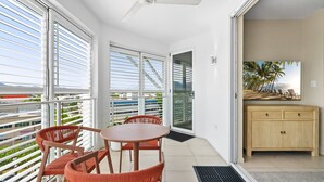 Ein Balkon mit Tisch und Stühlen, eine Schiebetür und Blick auf Palmen.