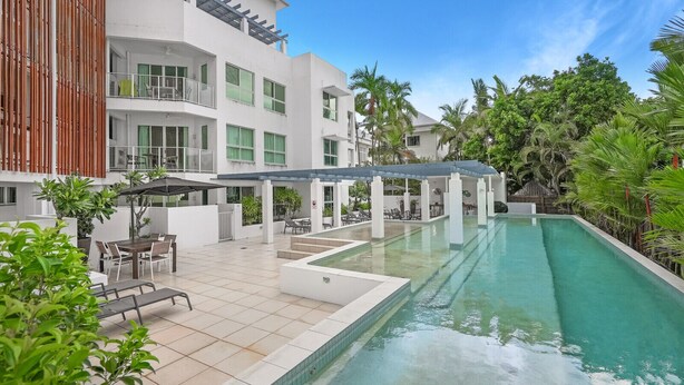 A modern hotel with a swimming pool, outdoor seating, and lush greenery.