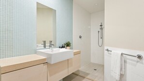 A modern bathroom with a white sink, a mirror, and a shower area.