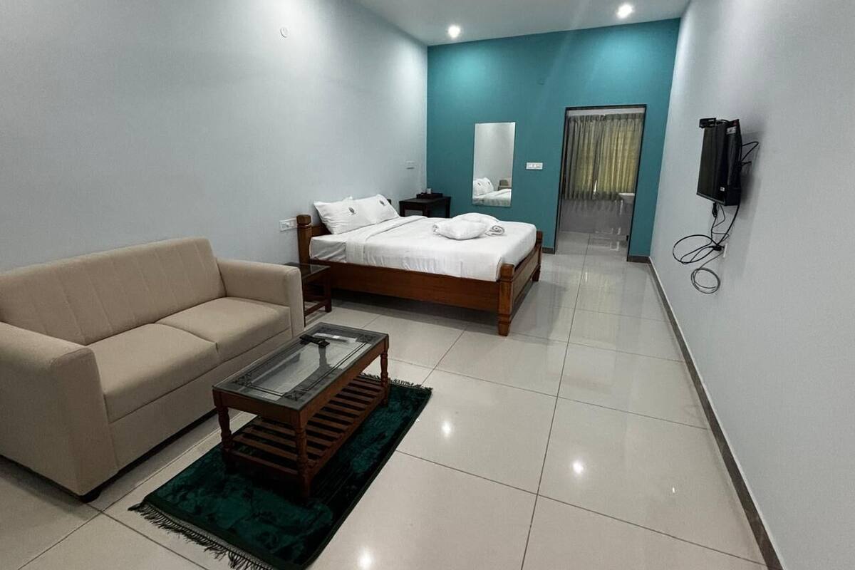 A modern hotel room with a bed, a sofa, a coffee table, a ceiling fan, and a TV.