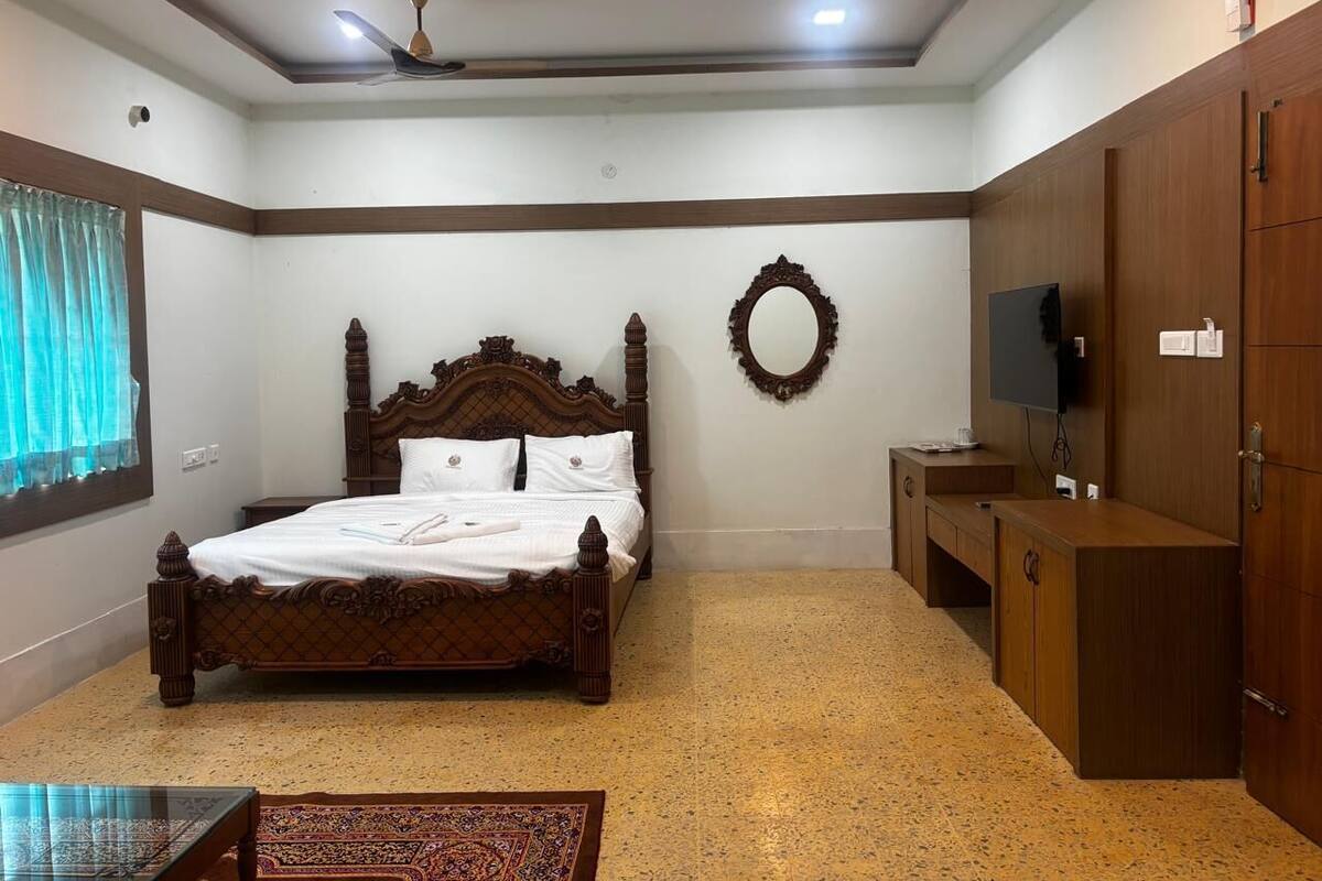 A bedroom with a wooden bed, a television, a wardrobe, and a small table.
