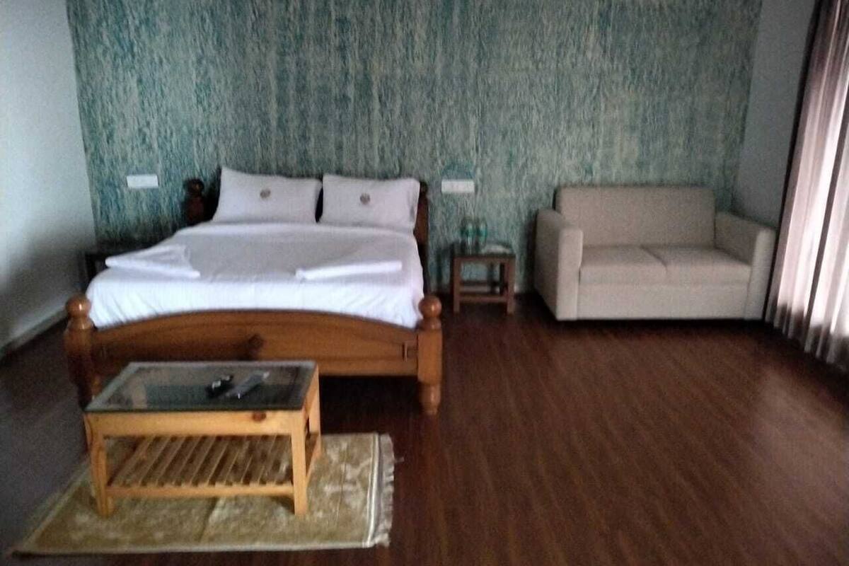 A room with a wooden bed, a glass-top coffee table, a beige sofa, and a patterned wall.