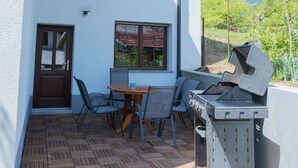 Eine Terrasse mit Grill, Stühlen und Tisch.