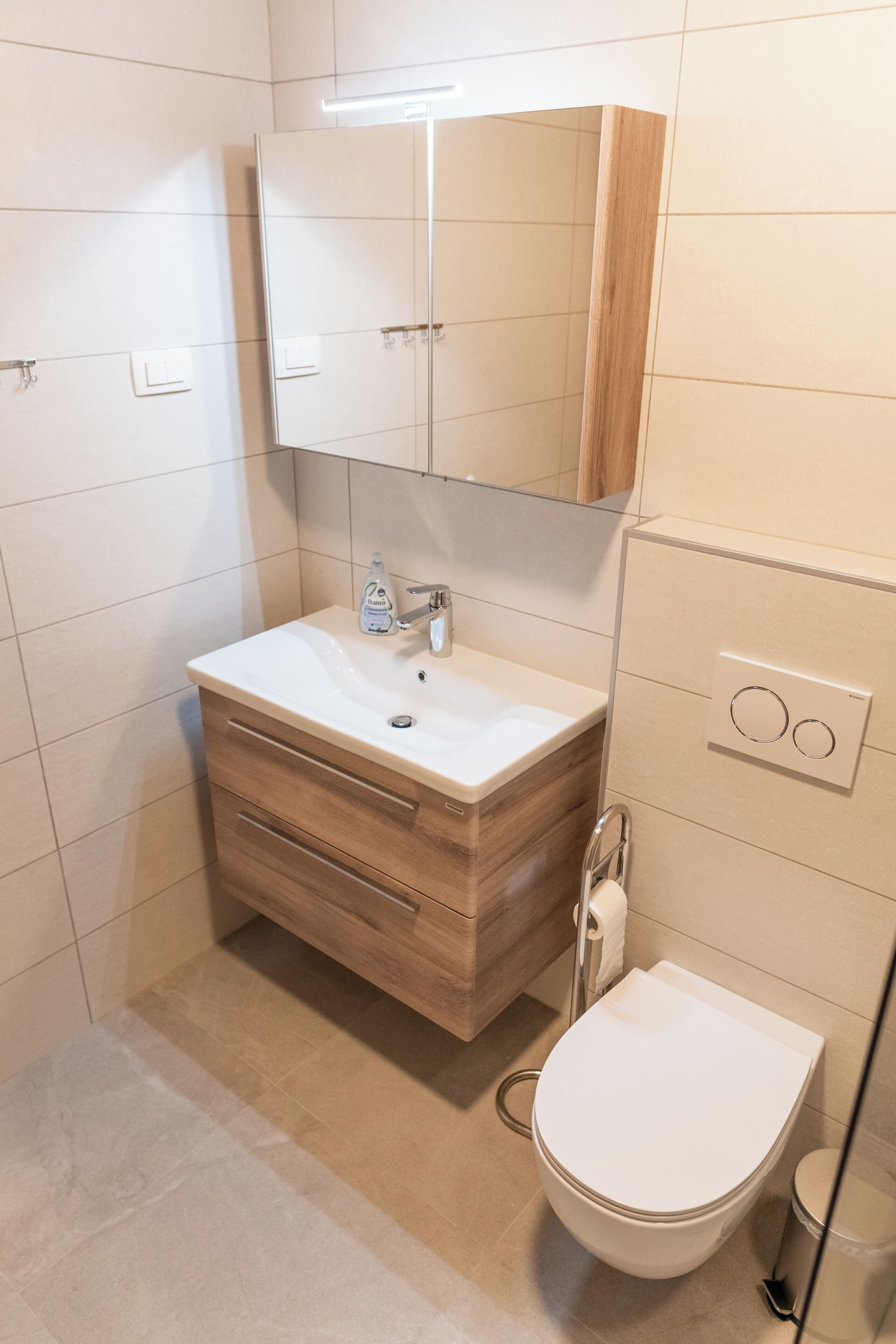 Et moderne badeværelse med en hvid vask, trækommode, et spejl og et toilet.