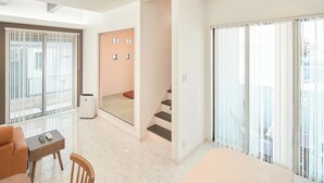 A modern hotel room with a large sliding glass door, a sofa, a small table, and a staircase leading to an upper floor.