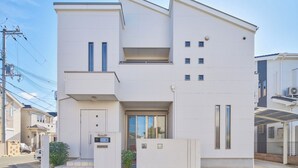 A modern two-story residential building with a flat roof, large windows, and a small balcony.