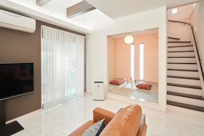A modern living room with a flat-screen TV, a sofa, a coffee table, and a large mirror reflecting the room.
