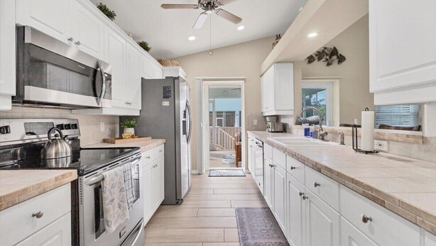 A modern kitchen with white cabinetry, stainless steel appliances, and a view to the backyard.