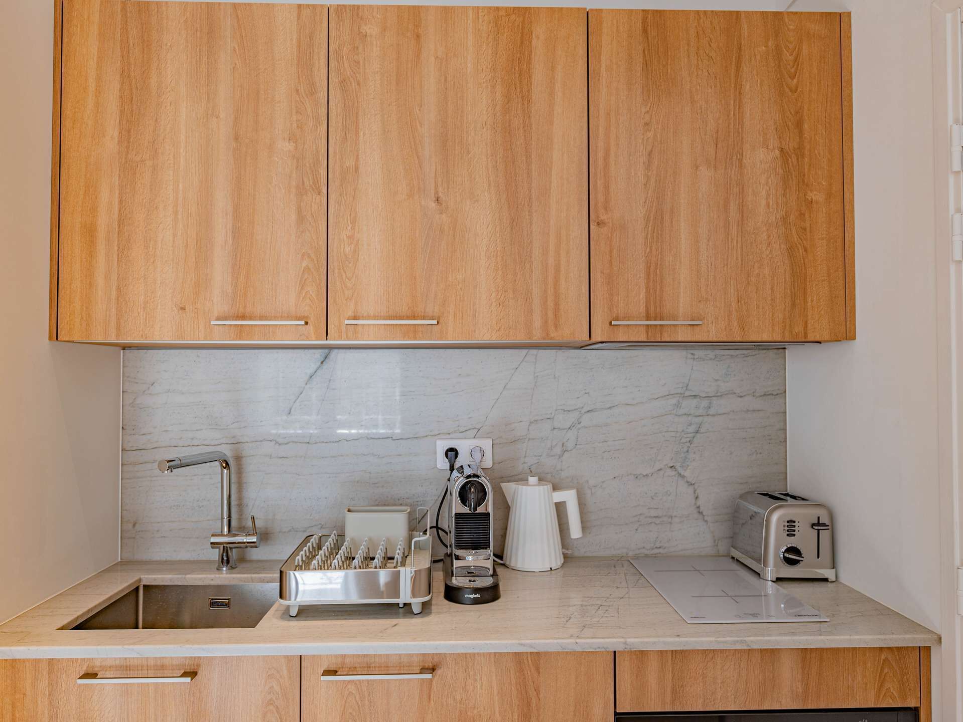 Una cocina con armarios de madera, salpicadero de mármol, un lavamanos, una cafetera, un tostador y un lavavajillas.