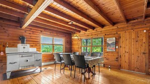 Uma cabana de madeira com uma mesa de jantar e cadeiras, uma área de cozinha e janelas amplas.