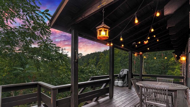 Um deck de madeira com mesa e cadeiras, rodeado por um corrimão, com vista para uma área arborizada.