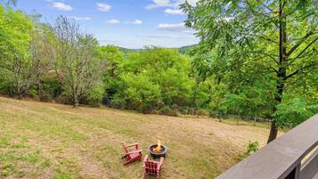 A grassy outdoor area with a fire pit and two red Adirondack chairs.