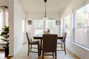 A dining area with a table and four chairs, large windows, and a hanging light fixture.
