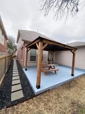 A wooden patio with a picnic table, surrounded by a brick wall and a wooden fence.