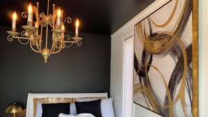 Un dormitorio con una araña, una cama con ropa de cama blanca y negra, y un cuadro abstracto grande en la pared.