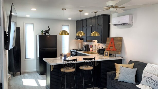 Una cocina moderna con armarios oscuros, una isla central con taburetes de bar, iluminación colgante y un ventilador de techo.
