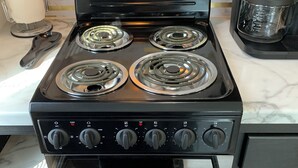 Una cocina con estufa negra, cuatro hornillas y una cafetera.
