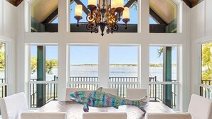 A dining area with a table set for four, a chandelier, and large windows overlooking a body of water.